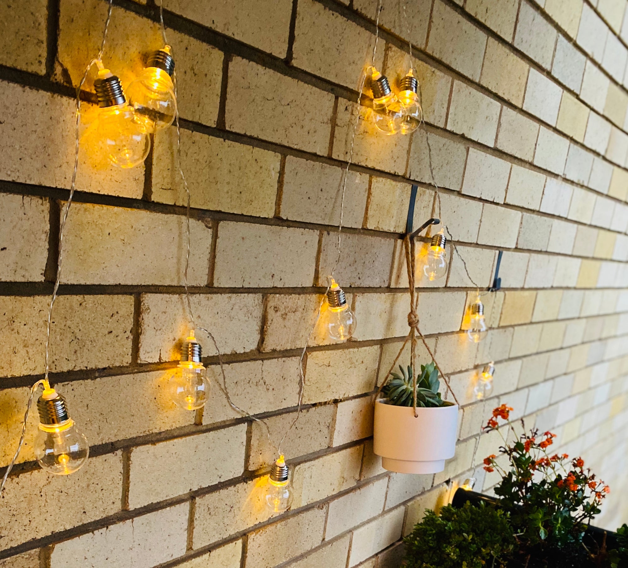 String lights and plants hanging on the brick wall using the Brick Grips' Brick Hanger to support without damaging the wall.
