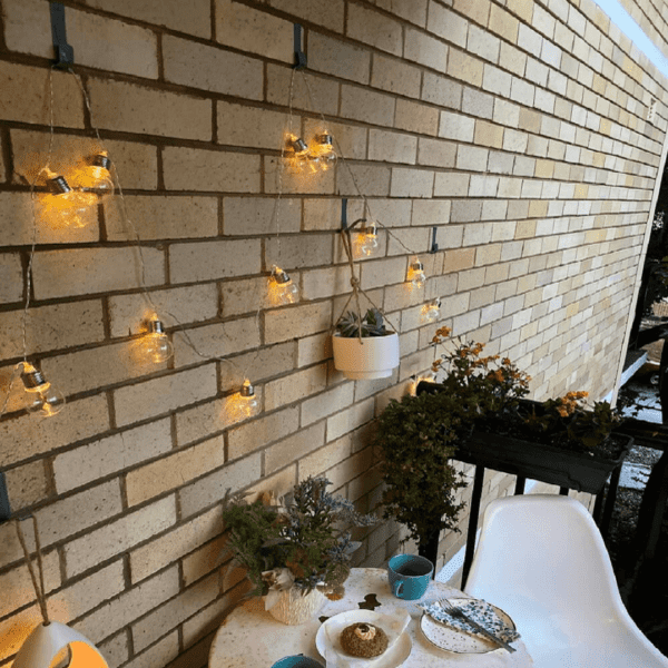 Five brick hooks hanging on the brick wall with string lights and plants